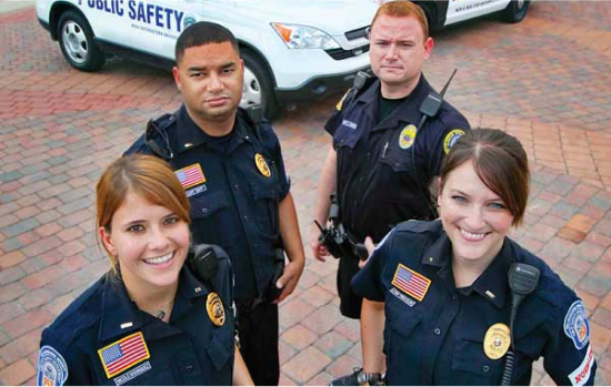 Criminal Justice graduates in uniform standing in front of public safety vehicles.
