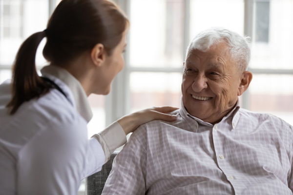 Caring geriatric nurse in white coat cares for grey-haired elderly man in nursing home
