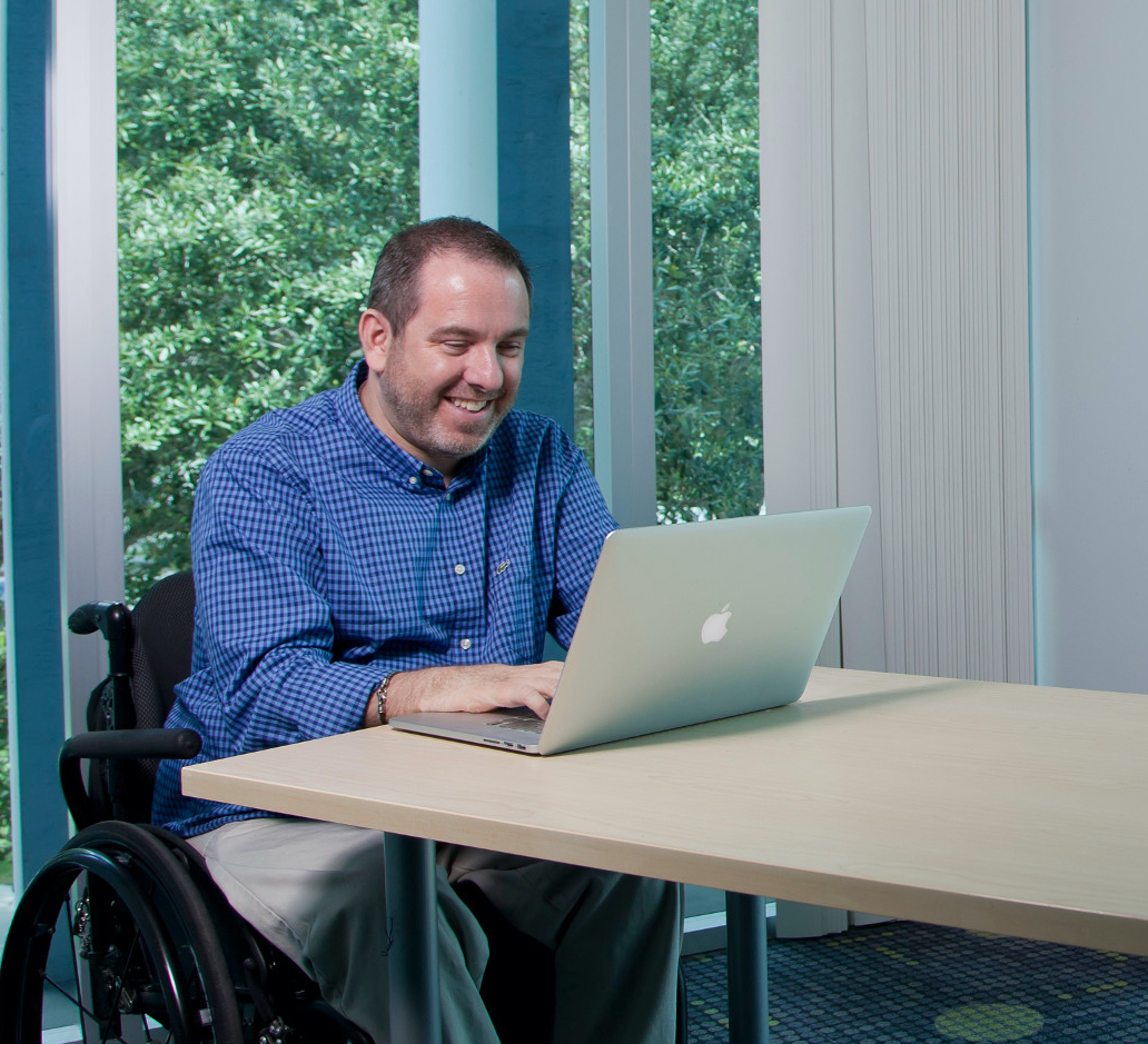 man in a wheelchair seated at a table using laptop computer