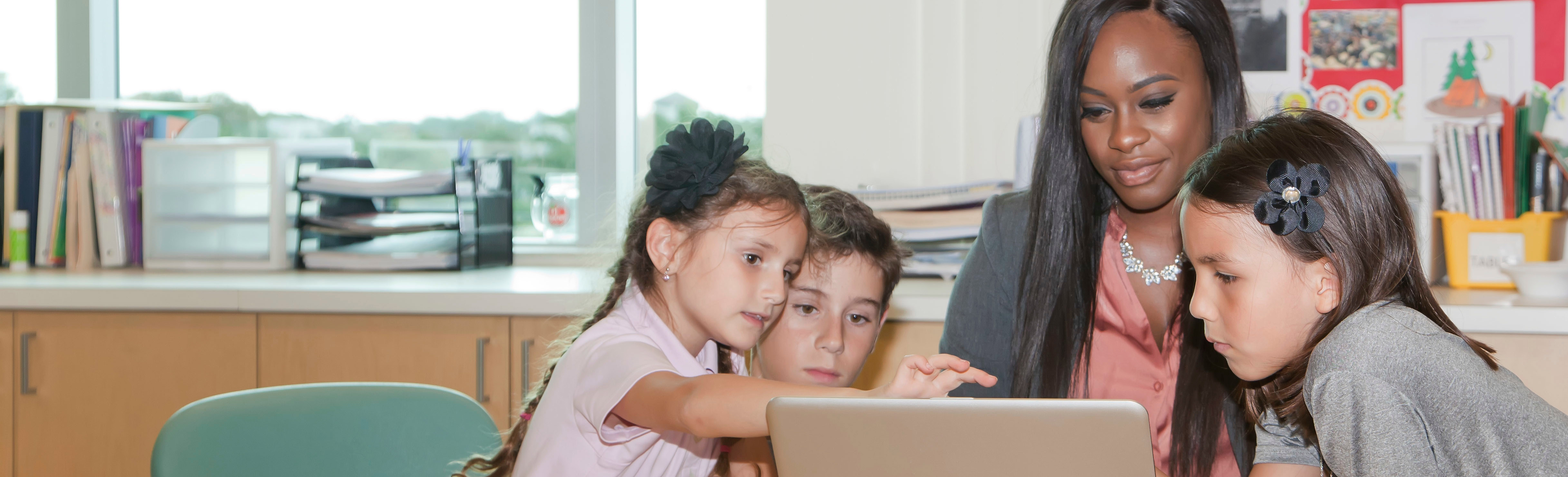 teacher and young students looking at a laptop